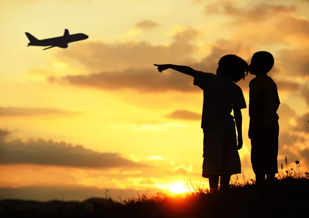 Two kids silhouette on meadow looking at airplane